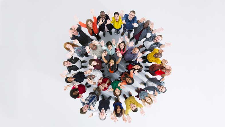 Diverse group of people standing in a circle and looking up at an overhead camera and waving