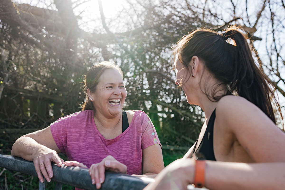 Two women smiling in a park wearing workout clothes